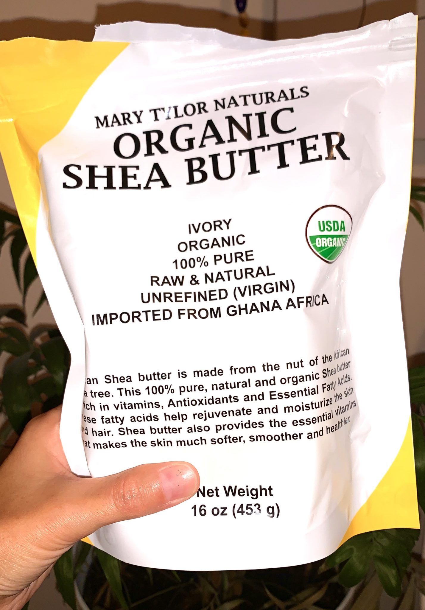 Photo of a hand holding a white and yellow plastic bag of Mary Tylor Naturals' Organic Shea Butter